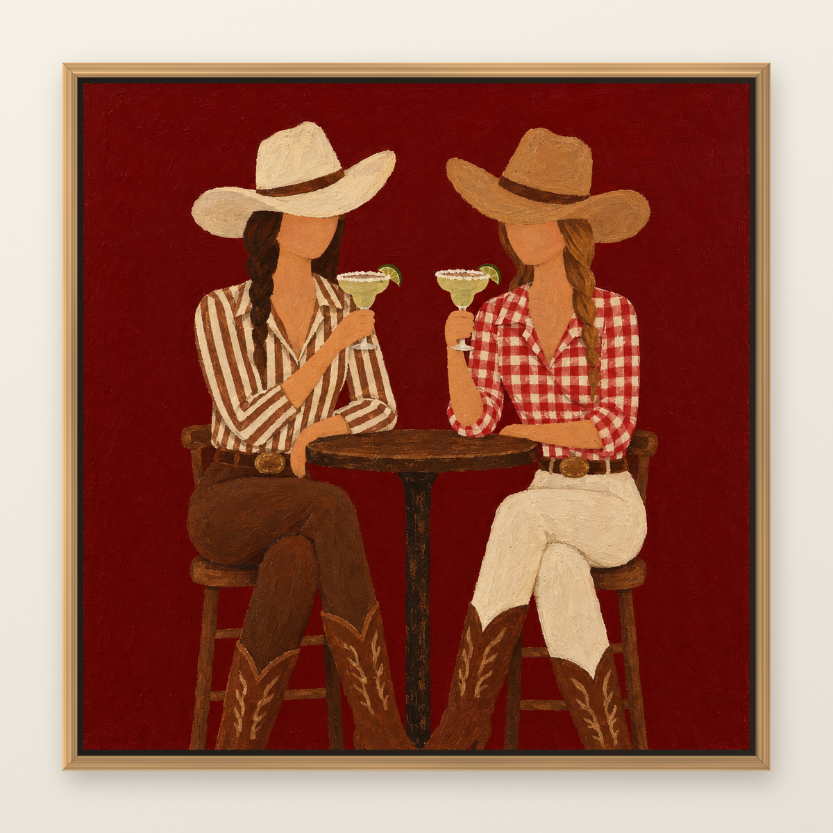 Western folk art oil painting of two cowgirls toasting margaritas, shown in a slim oak floater frame on a warm white wall